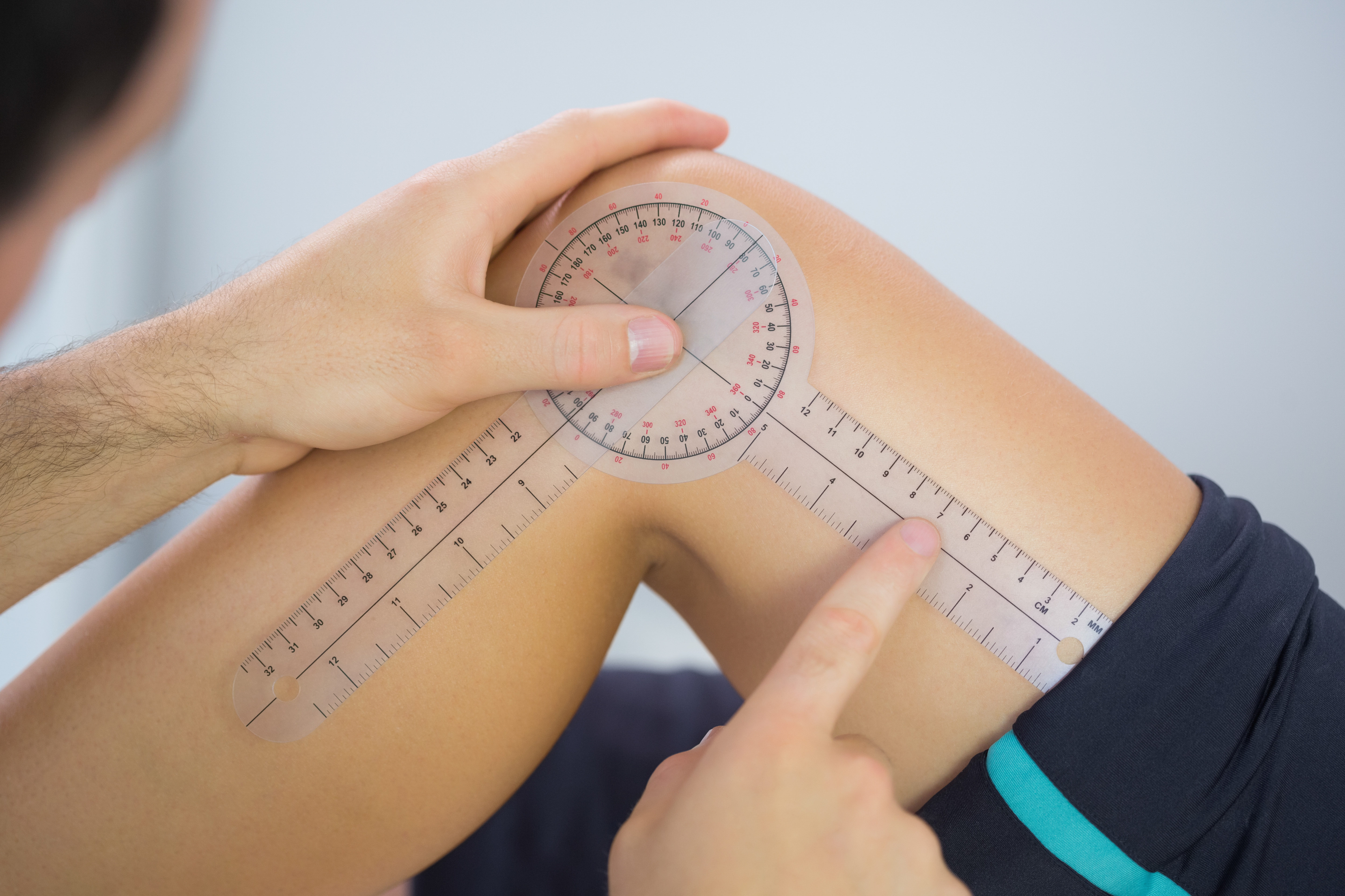 Physiotherapist examining knee angle with goniometer in bright office